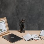 Mesa de advogado com documentos jurídicos, laptop, lupa e estátua da Justiça.