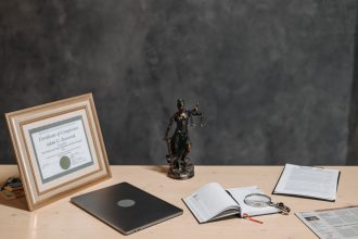 Mesa de advogado com documentos jurídicos, laptop, lupa e estátua da Justiça.