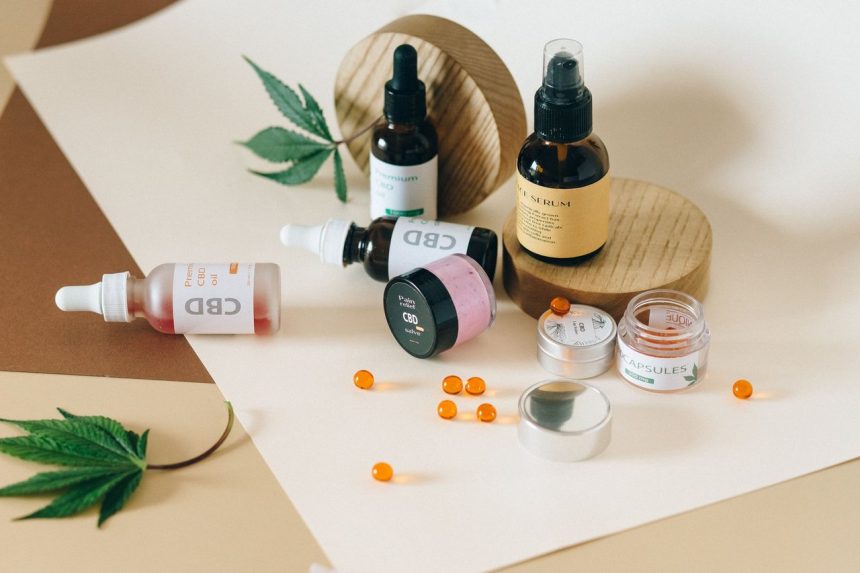 Frascos de óleo, cápsulas e outros produtos de canabidiol dispostos sobre fundo neutro, acompanhados de folhas de cannabis.