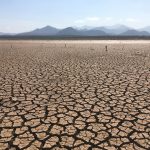 Paisagem extensa de solo profundamente rachado sob céu claro, caracterizando condições severas de seca.