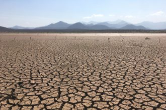 Paisagem extensa de solo profundamente rachado sob céu claro, caracterizando condições severas de seca.