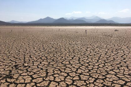 Paisagem extensa de solo profundamente rachado sob céu claro, caracterizando condições severas de seca.
